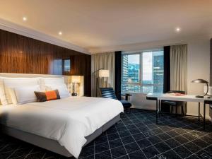 悉尼Swissotel Sydney的酒店客房设有一张大床和一张书桌。