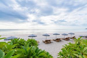 华欣瓦兰达洛奇酒店的海滩上设有桌子和遮阳伞,还有大海
