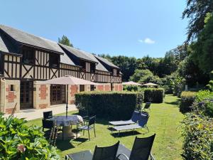 Sainte-Marie-au-BoscLe manège Gite Le Tilleul的院子里的房屋,配有椅子和遮阳伞