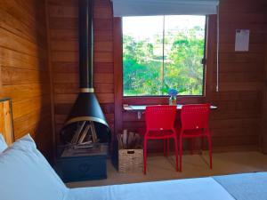 维奥康德马奥Refúgio Allamanda Flats的一间卧室配有桌子、两把红色椅子和一个壁炉