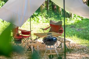 白马村森之小木屋的帐篷下的带烧烤架和椅子的野餐桌