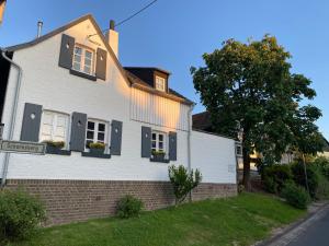 博恩海姆Scheunentraum Brenig的白色的房子,有黑色百叶窗和一棵树
