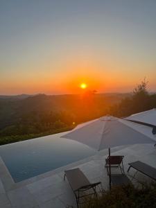 GolferenzoBorgo dei Gatti Albergo Diffuso的一个带遮阳伞和椅子的游泳池,享有日落美景