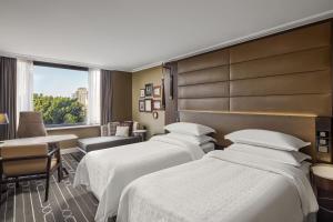 悉尼Sheraton Grand Sydney Hyde Park的酒店客房设有三张床和窗户。