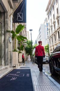雅典Athens The L7 Str - Luxury Boutique Collection Hotel的身穿红衬衫和帽子的人在街上走