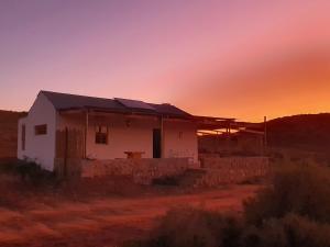 奥茨胡恩Klein Doorn Farm Stay的沙漠中的房屋,背景是日落