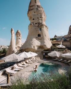 格雷梅Aza Cave Cappadocia Adult Hotel的坐在游泳池里的女人,带椅子和遮阳伞