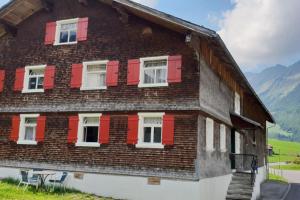 布雷根茨沃尔德地区奥Great old WÄLDERHAUS的一座带红色百叶窗和山脉的木屋