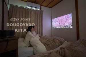 松山GUEST HOUSE DOUGOYADO KITA - Vacation STAY 14923的一位女士躺在卧室的床上,卧室里配有电视