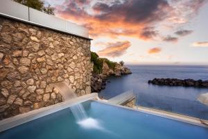 伊斯基亚伊斯基亚蓝光度假酒店的蓝色游泳池,毗邻一座石头建筑和大海