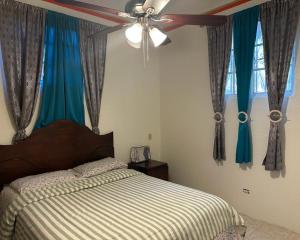海地角La Difference Guest House的一间卧室配有一张带蓝色窗帘的床和吊扇