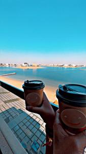 阿尔科兰منتجع اووه يامال البحري في الخيران OOh Yaa Mal的水前拿着两个咖啡杯的人