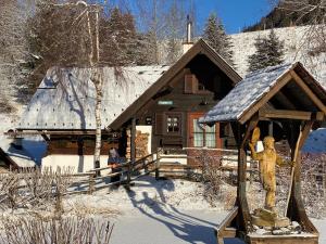 多内尔斯巴赫瓦尔德Fischerhütte Donnersbachwald的雪地中的小木屋,前面有雕像