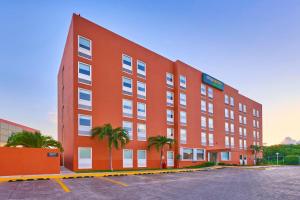 坎昆City Express Junior by Marriott Cancun的停车场内一座棕榈树的大型红色建筑