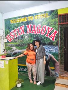 武吉拉旺Ustin Nagoya Bukit Lawang jungle Trekking tours&transport book with us的两名妇女站在欢迎来酒店标志前