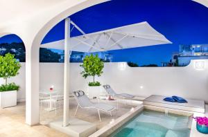 卡普里Pazziella Garden & Suites的一个带白色遮阳伞和椅子及桌子的游泳池