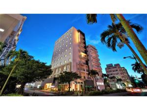 那霸Y's Inn Naha Oroku Ekimae - Vacation STAY 25852v的棕榈树城市街道上的一座高楼