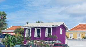 威廉斯塔德Purple house in colorful city centre的一座紫色的房子,前面有车停放