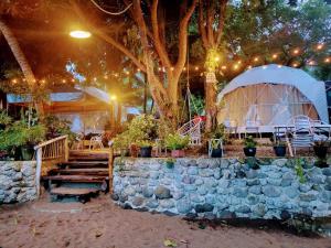 道因Glamping Dome Dauin Beach Resort的一个带石墙、一棵树和帐篷的庭院