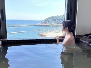 热海热海美景私人温泉公寓式酒店的坐在浴缸里,欣赏海洋美景的女人