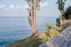 RubavuMAISON DU LAC -Feel home with opening on Lake Kivu的坐在水边的树下的一个女人