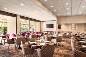 肯纳新奥尔良机场希尔顿逸林酒店的一间设有桌椅的餐厅,位于带窗户的房间内