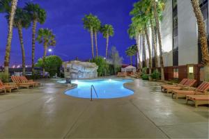 拉斯维加斯Hampton Inn Tropicana的游泳池,晚上有椅子和棕榈树