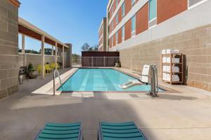 斯泰茨伯勒Home2 Suites By Hilton Statesboro的一座带蓝色椅子的游泳池,位于大楼旁