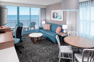 弗吉尼亚海滩弗吉尼亚海滨海滩/南万怡酒店的带沙发和桌子的客厅以及带阳台的客房。