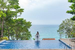 卡伦海滩Secret Cliff Resort & Restaurant - SHA Plus的站在游泳池边俯瞰大海的女人
