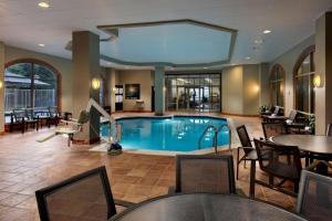 奥斯汀Embassy Suites by Hilton Austin Arboretum的酒店大堂的游泳池,配有桌椅
