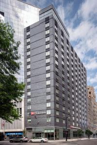 皇后区Hilton Garden Inn Long Island City的一座灰色的大建筑,前面有汽车停放