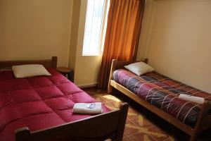 库斯科库斯科行囊旅舍的宿舍间的两张床,配有红色床单和窗户