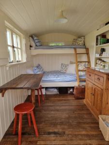 科姆堡The Delkin Shepherds Huts Castle Combe的客房设有一张桌子和一张双层床。
