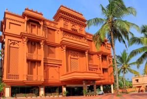 阿勒皮Haveli Backwater Resort的一座橘色的建筑,前面有棕榈树