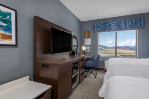 科迪Hampton Inn & Suites Cody, Wy的酒店客房配有一张床和一张书桌及一台电视