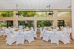 惠蒂尔惠蒂尔希尔顿逸林酒店的宴会厅配有白色的桌椅和大窗户