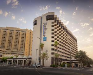 迪拜迪拜德伊勒河丽笙酒店的一座高大的白色建筑,位于一条种有棕榈树的城市街道上