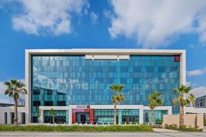 迪拜Radisson RED Dubai Silicon Oasis的一座大型玻璃建筑,前面有棕榈树