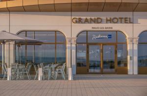 敦刻尔克Radisson Blu Grand Hotel & Spa, Malo-Les-Bains的外面设有桌椅的大酒店