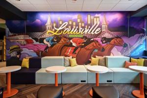 路易斯威尔Tru By Hilton Louisville Airport的餐厅内壁画,配有桌子和凳子
