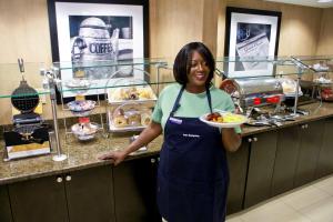 夏洛特汉普顿酒店及套房 - 夏洛特机场的一位在厨房里拿着一盘食物的妇女
