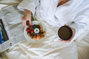 柏林路易莎故居酒店的床上的女人,有盘子的食物和一杯咖啡