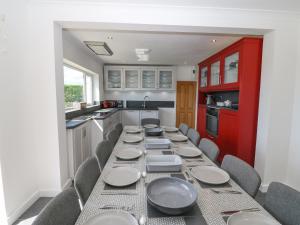AberffrawGlanffraw的厨房配有长桌子、椅子和红色橱柜