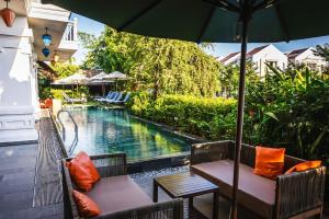 会安Hoi An Odyssey Hotel & Spa的一个带两把椅子和一把遮阳伞的庭院,毗邻一个游泳池