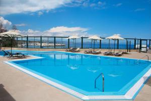 马蒂Ramada by Wyndham , Athens Club Attica Riviera的一个带椅子和遮阳伞的大型蓝色游泳池