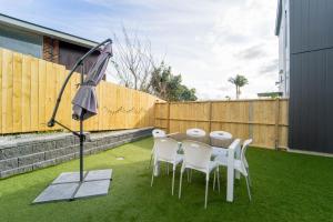 奥克兰Modern Sunnyhills Town House的一张桌子、白色的椅子和一把雨伞,放在草地上