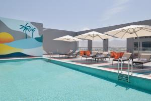 马斯喀特Aloft Muscat的大楼内一个带椅子和遮阳伞的游泳池