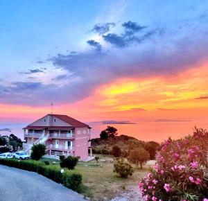 圣斯特凡诺斯Nikos Apartments Corfu的粉红色的建筑,背景是日落