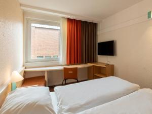 杜伊斯堡B&B Hotel Duisburg Hbf-Nord的酒店客房设有两张床、一张书桌和一个窗户。